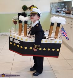 a young boy dressed as a captain holding a model ship made out of cardboards