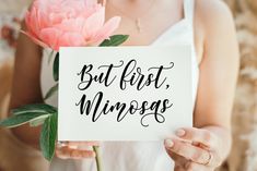 a woman holding a pink flower and a sign with the words but first, minds