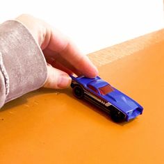 a toy car being held by someone's hand on top of a wooden table