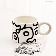 a black and white coffee cup sitting on top of a table next to a drawing