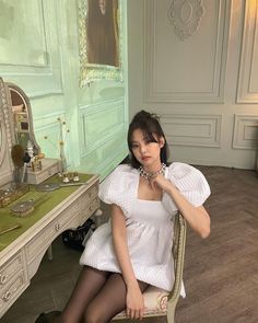 a woman sitting on a chair in front of a desk with a mirror and dressing table