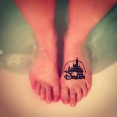 a person with a disney tattoo on their foot is standing in the water and has her feet crossed