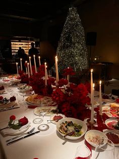 a long table is set with food and lit candles for christmas dinner guests can be seen in the background