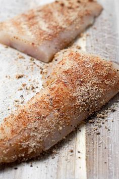 two fish fillets on a cutting board with seasoning sprinkled around them