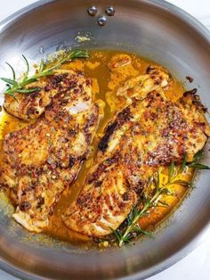 two pieces of chicken in a pan with sauce and herbs on the side, ready to be cooked