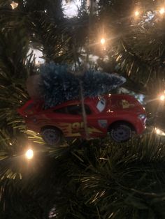 a red car ornament hanging from a christmas tree with lights on the branches