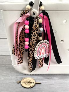 the leopard print and pink ribbon necklaces are hanging from a white tote bag