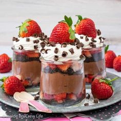 three desserts in glass jars with strawberries and chocolate chips on top, sitting on a plate