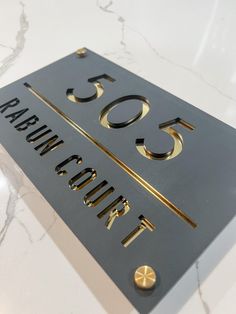 a close up of a metal sign on a marble surface with gold lettering and numbers