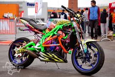 a colorful motorcycle parked on the street with people standing around it and in the background