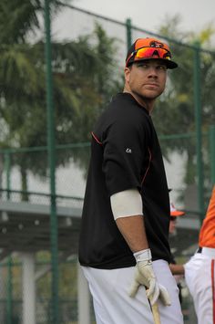 a man holding a baseball bat while standing next to another man wearing gloves and an orange visor