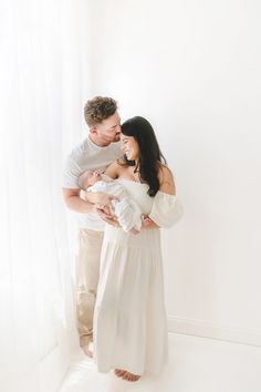 a man and woman holding a baby in their arms while standing next to a window