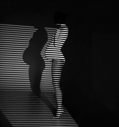 a woman standing in the dark with her shadow