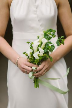 a woman in a white dress holding a bouquet of green and white flowers on her wedding day