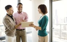 two men and a woman standing in an office looking at something on a clipboard