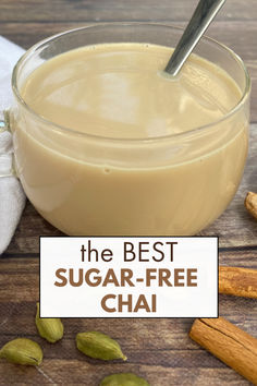 Creamy, sugar-free chai tea in a glass mug with a spoon next too cinnamon sticks and cardamom pods.