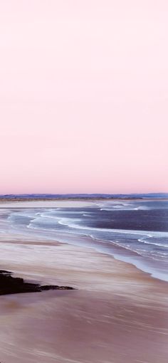 an ocean beach with waves coming in to the shore and people walking on the sand