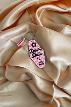 a pink and white keychain with the word aloha on it sitting on a satin surface