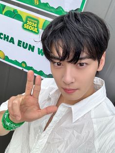 a young man making the peace sign with his hand while wearing a white shirt and green bracelet