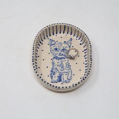 a small blue and white plate with a cat keychain on it's side