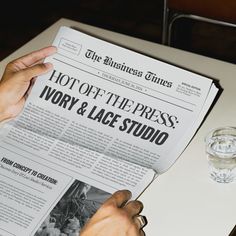 a person is reading a newspaper on a table next to a glass of water and two glasses