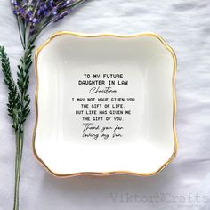 a white and gold plate with writing on it next to some purple flowers in the background