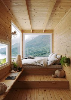 a bedroom with wooden walls and flooring has a large window that looks out onto the mountains