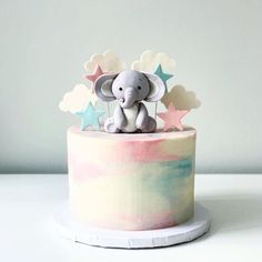 an elephant figurine sitting on top of a colorful cake with clouds and stars