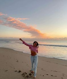 a woman standing on top of a sandy beach next to the ocean with her arms in the air