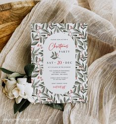 a white and red christmas party card on top of a bed next to a flower