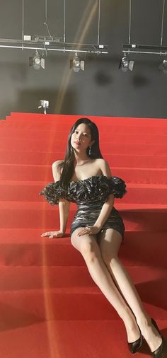 a woman sitting on top of a red carpet next to some stairs with her legs crossed