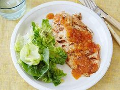 a white plate topped with meat and salad next to a glass of water on a table