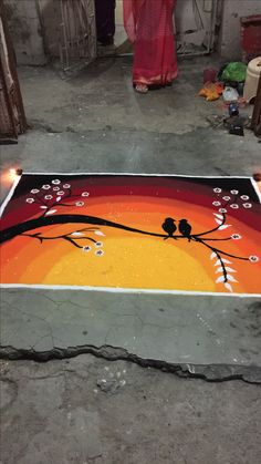 a painting on the ground with two birds sitting on it