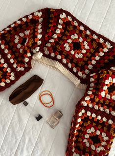 a crocheted sweater and other items are laid out on a white bed sheet