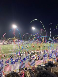 the crowd is watching fireworks and streamers in the air at a football game on a dark night