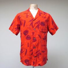 * Men's Hawaiian shirt c 1960s* Cotton fabric* Anthurium, Bird of Paradise, shields, and other tropical motifs in maroon on red background* Small spread collar * Single patch pocket* Back yoke has action pleats for comfort* Short, set-in sleeves are notched at hem* 5 coconut shell buttons* Squared-off hem with 2" side ventsMissing labelVery good condition. One minor repair has been made. A pinhole above the breast pocket was repaired by fusing fabric from inner seam. Virtually impossible to dete Red Retro Print Summer Shirt, Red Collared Hawaiian Shirt For Beach, Red Collared Hawaiian Top, Red Camp Collar Top With Tropical Print, Retro Red Short Sleeve Camp Shirt, Red Retro Shirt With Camp Collar, Vintage Red Camp Shirt With Camp Collar, Retro Red Shirt With Camp Collar, Red Tropical Print Top With Camp Collar