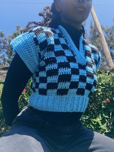 a woman wearing a blue and black crocheted vest with a baseball bat in her hand