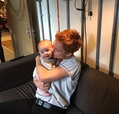 a man holding a baby in his arms while sitting on a couch next to a wall