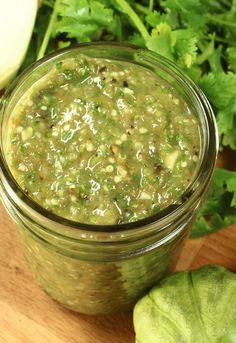 a glass jar filled with green salsa sitting on top of a wooden table next to lettuce