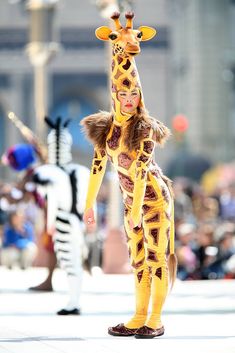 a woman in a giraffe costume walking down the street with other people behind her