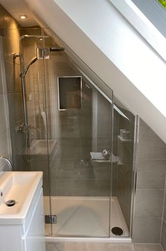 a bathroom with a walk in shower next to a white sink and toilet under a slanted ceiling