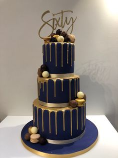 a three tiered blue and gold cake with chocolate candies on the bottom layer