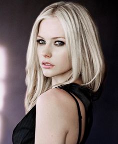 a woman with blonde hair and blue eyes posing for a photo in front of a dark background