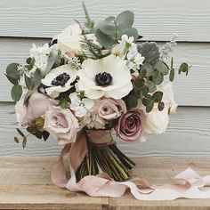 a bridal bouquet with white and pink flowers on a wooden table next to a wall