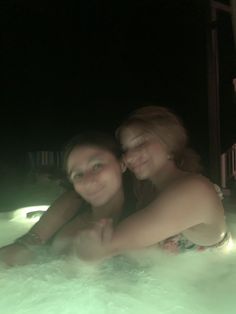 two women are in the bathtub at night with their arms around each other and smiling