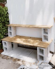 a bench made out of cinder blocks sitting on the side of a building next to a tree