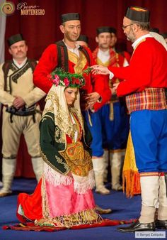 a man and woman dressed in traditional costume standing next to each other on stage with others behind them