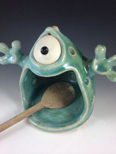 a frog figurine with a spoon in it's mouth and eyes open