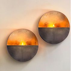 two circular metal wall lights with lit candles in the middle on a white wall next to each other