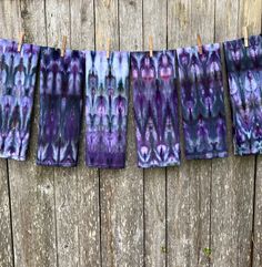 five pieces of cloth hanging on clothesline next to wooden planks, with purple and green designs